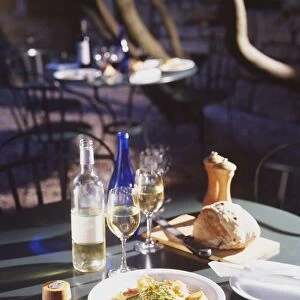 A dinner consisting of a plate of bread, a fish and vegetable dish accompanied by a bottle of white wine and two glasses