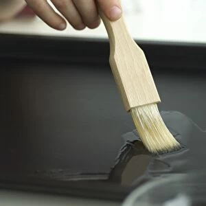 hand brushing oil over baking tray